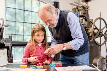 Spürnasen-Rallye Ein älterer Mann zeigt einem neugierigen Mädchen Modelle in einem industriellen Museumsumfeld.