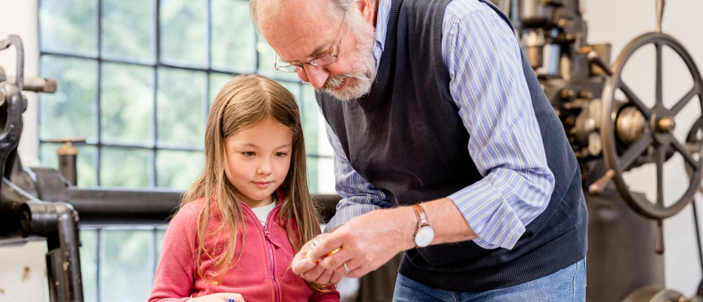 Spürnasen-Rallye Ein älterer Mann zeigt einem neugierigen Mädchen Modelle in einem industriellen Museumsumfeld.