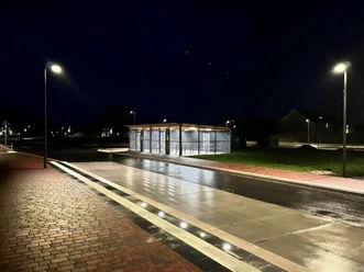 Fahrradstation am Dock Beleuchtete Fahrradstation mit überdachten Abstellplätzen an einer nassen Straße in der Nacht