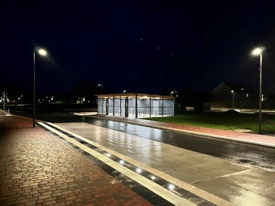 Fahrradstation am Dock Beleuchtete Fahrradstation mit überdachten Abstellplätzen an einer nassen Straße in der Nacht