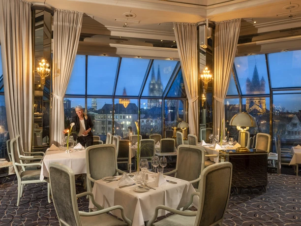 An elegant, glass-enclosed restaurant lounge with set tables and a panoramic view at dusk.