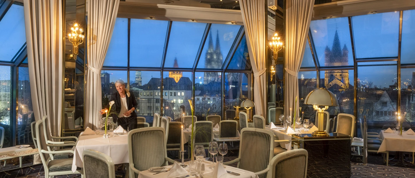 KOL_215_Restaurant-Bellevue.jpg An elegant, glazed restaurant lounge with set tables and panoramic views at dusk.