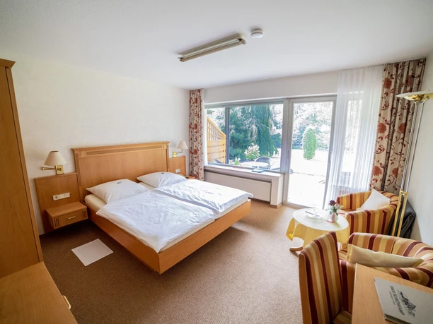 Haus Berkenkamp-Doppelzimmer.jpg Doppelzimmer mit Holzinterieur, großem Bett, Sitzbereich, sonnendurchfluteten Fenstern und Gartenblick.