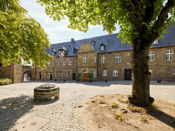 Schloß Broich, Mülheim an der Ruhr <p>Historischer Innenhof mit Brunnen, von Bäumen umgeben und mit Steinpflaster ausgelegt.</p>
