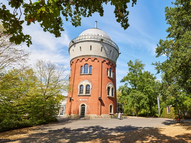 Camera Obscura, Mülheim an der Ruhr Roter Backsteinturm der Camera Obscura in Mülheim, umgeben von grünen Bäumen unter blauem Himmel.