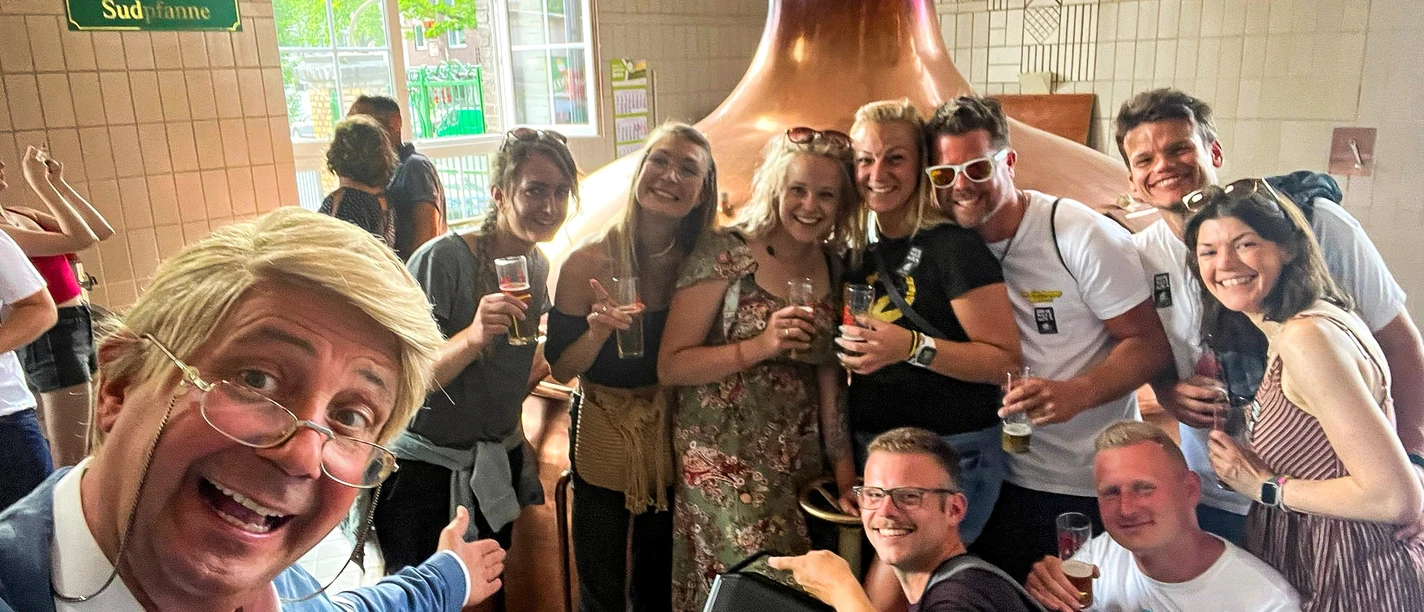 comedy-fuehring-hajo.jpg Menschen feiern lachend in einer Brauerei, umgeben von Kupferkesseln und mit Biergläsern.</p>