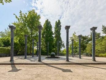 Ringlokschuppen Ruhr, Mülheim an der Ruhr Steinkreis mit hohen Säulen im Freien, umgeben von Bäumen und hellem Himmel mit Wolken.
