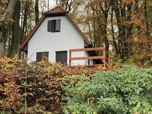 Freilichtbühne Nettelstedt Ein weißes Haus mit Schindeldach steht umgeben von herbstlichem Laub im Wald und vermittelt Ruhe.