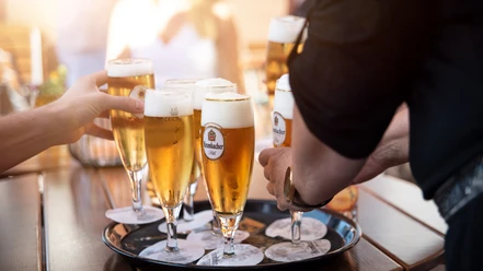 Gaststaette Zum Hoelzchen Tablett mit Bierglaesern.jpg Sechs Personen stoßen mit vollen Biergläsern auf einem Tablett im Freien an.