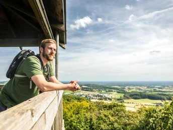 Ein Mann steht auf dem Luisenturm und genießt den weiten Blick über die bewaldete Landschaft.