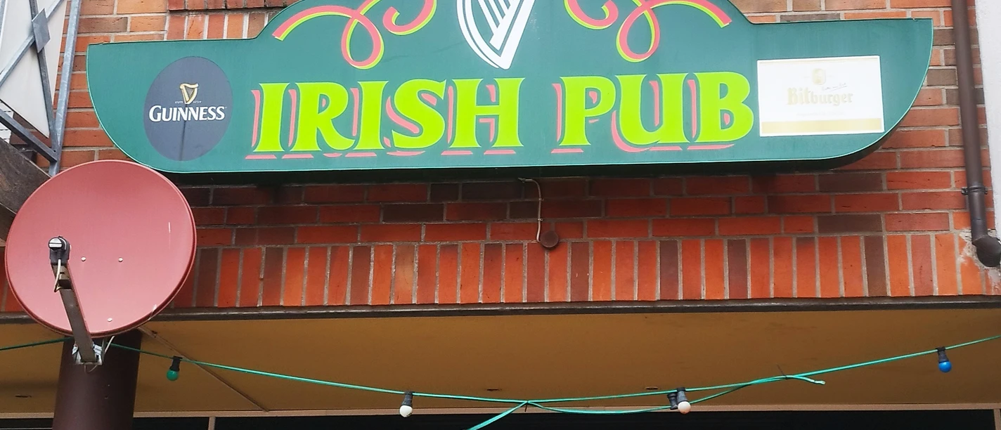 Irish-Pub_Spelle©SG-Spelle.jpg Grünes Schild mit gelber Aufschrift Irish Pub und Logos von Guinness und Bitburger an roter Backsteinwand.