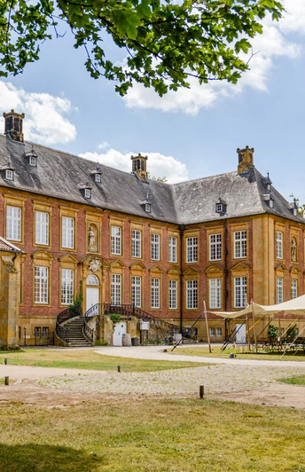 Barockes Schloss mit Backsteinfassade, großen Fenstern, Zeltpavillon und Garten, umgeben von Bäumen.
