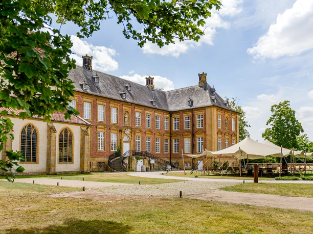 Kloster Marienfeld | Teutoburger Wald | Harsewinkel Barockes Schloss mit Backsteinfassade, großen Fenstern, Zeltpavillon und Garten, umgeben von Bäumen.