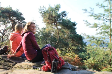 Ibbenbüren_Plisseefelsen_Stadtmarketing Ibbenbüren GmbH_SPL_2000.jpg Zwei Personen sitzen entspannt auf einem Felsen, umgeben von grünen Bäumen und genießen den Ausblick.
