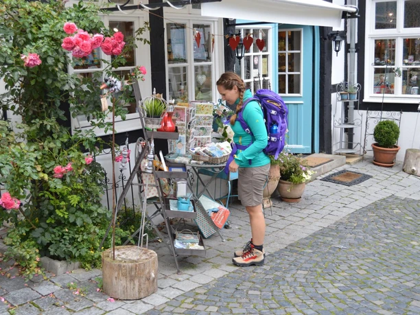 Tecklenburg_Innenstadt_Julia_Bohlken.jpg Eine Wanderin mit lila Rucksack betrachtet einen Flohmarktstand in einer gepflasterten Altstadtgasse.