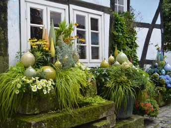 Üppig bepflanzte Steinstufen vor einem Fachwerkhaus mit dekorativer Keramik im Vordergrund.