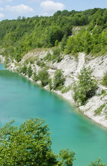 Blick auf eine türkisfarbene Schlucht, umgeben von grünen bewaldeten Hügeln unter blauem Himmel.