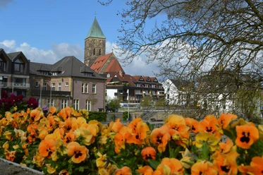 Rheine_Emsufer_Foto_Teutoburger Wald Tourismus_I Bohlken_1600.jpg Blick auf blühende orangefarbene Blumen mit einer beeindruckenden Kirche im Hintergrund, leicht bewölkter Himmel.