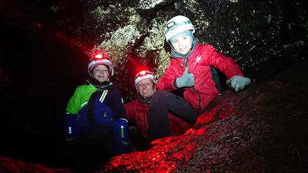 Drie mensen met helmen en hoofdlampen verkennen een donkere grot omgeven door rotswanden.