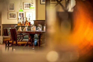 Restaurant Tilia im Hotel Lindenhof Gemütlich gedeckter Tisch in einem Restaurant mit Holzmöbeln, Gläsern, Flaschen und grünen Hängelampen im Hintergrund, warme Atmosphäre.