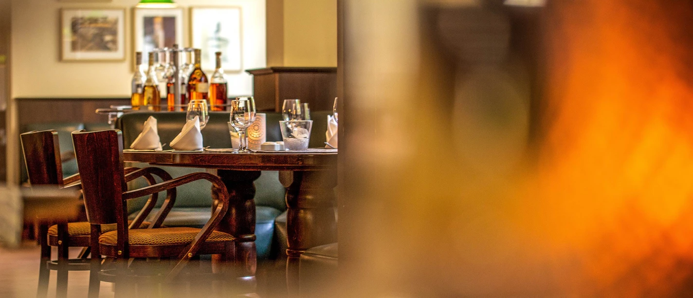 Restaurant Tilia im Hotel Lindenhof Gemütlich gedeckter Tisch in einem Restaurant mit Holzmöbeln, Gläsern, Flaschen und grünen Hängelampen im Hintergrund, warme Atmosphäre.