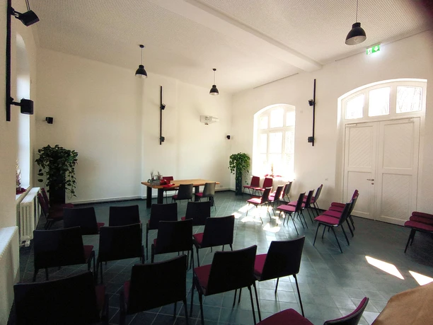 Kultur-Bahnhof-Morsbach Heller Veranstaltungsraum mit Stuhlreihen, Pflanzen, hölzernem Tisch vor großer Fensterfront.