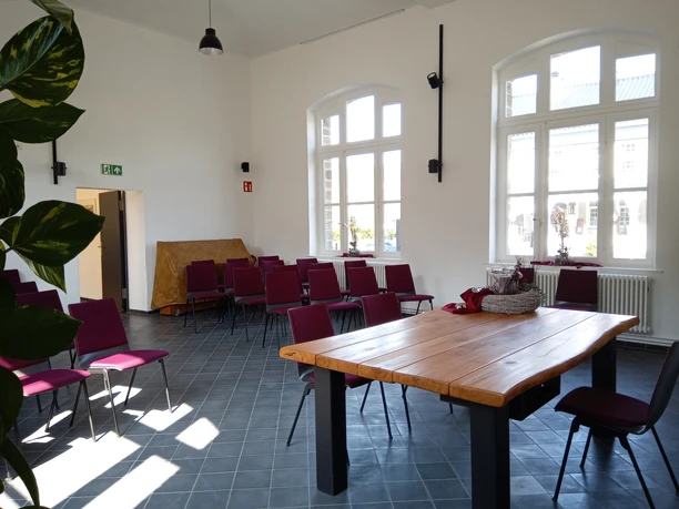 Kultur-Bahnhof-Morsbach Ein heller Seminarraum mit großen Fenstern, roten Stühlen und einem Holztisch, der viel Tageslicht empfängt.