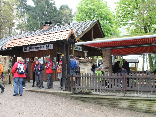 Dörenther Klippen_Almhütte_Teutoburger Wald Tourismus.JPG Eine Gruppe Wanderer versammelt sich vor einer Almhütte mit Biergarten im Teutoburger Wald.