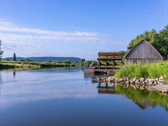 Schiffmühle Minden Eine historische Schiffmühle steht am ruhigen Flussufer, umgeben von üppiger Landschaft.