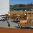 Hofladen Außenbereich Sonniger Außenbereich eines Cafés mit Holztischen und Stühlen, Zaun und ländlicher Landschaft im Hintergrund.