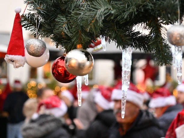 Merry X - Mas everybody! Weihnachtlich geschmückter Tannenbaum, Menschen mit Weihnachtsmützen im Hintergrund.