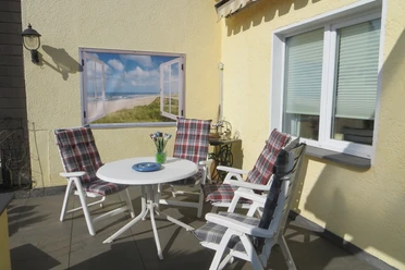 Sonniger Terrasse mit vier gestreiften Stühlen um einen weißen Tisch, Fenster zeigt Strandlandschaft.