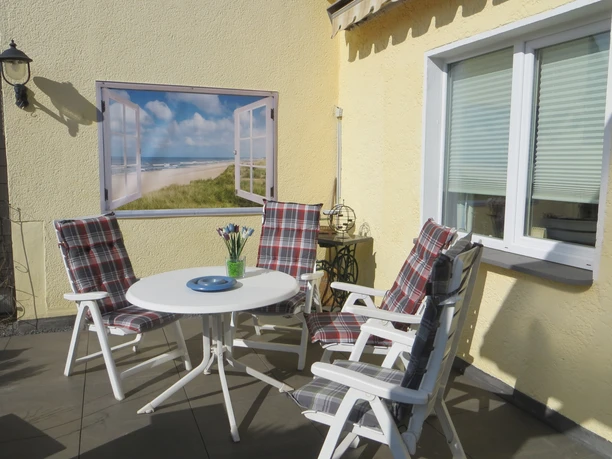 IMG_3825.JPG Sonniger Terrasse mit vier gestreiften Stühlen um einen weißen Tisch, Fenster zeigt Strandlandschaft.