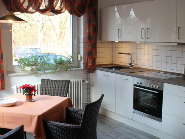 Eine moderne Küche mit weißen Schränken und einem Essbereich. Der Tisch ist mit einer orangenen Tischdecke und einer Weihnachtsdeko geschmückt.