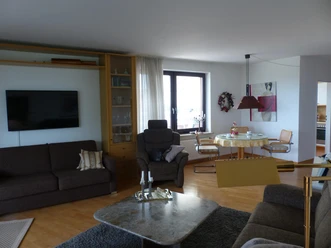 Wohnbereich der Suite mit Sofas, TV, Sessel, Esstisch und Küchenblick