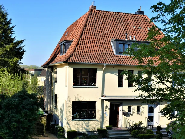Helle Hausfassade mit rotem Ziegeldach, Gauben und grünem Garten in Bad Salzuflen
