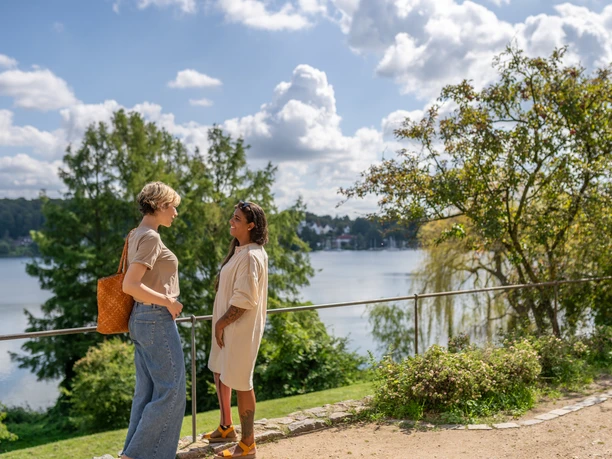 Zwei Frauen stehen am Ufer des Domsees in Ratzeburg und genießen das sommerliche Wetter.