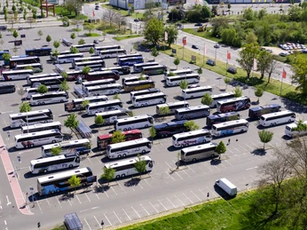 Buslogistik I Ein Parkplatz voller Reisebusse, in Reihen geparkt, von oben gesehen. Bäume und Gebäude im Hintergrund.A parking lot full of coaches, parked in rows, seen from above. Trees and buildings in the background.