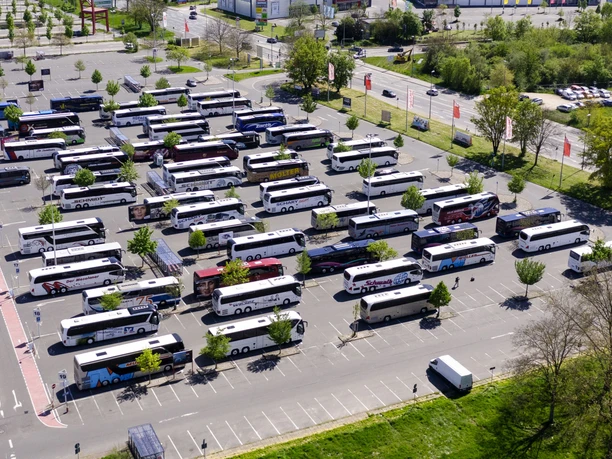 Buslogistik I A parking lot full of coaches, parked in rows, seen from above. Trees and buildings in the background.