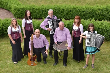 Bimmelbah Musikanten Eine Gruppe Musiker in traditioneller Kleidung spielt fröhlich auf Wiese, lächelnd zusammensstehend.