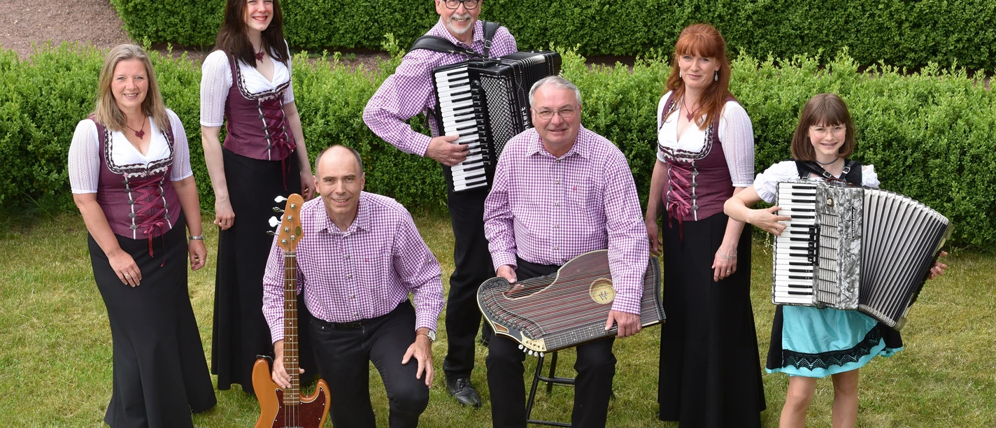 Bimmelbah Musikanten Eine Gruppe Musiker in traditioneller Kleidung spielt fröhlich auf Wiese, lächelnd zusammensstehend.