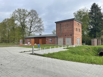 Backsteingebäude mit barrierefreiem Zugang, umgeben von Grünflächen und Informationstafeln.