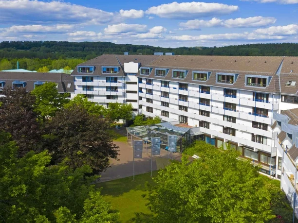 Blick auf die Caspar Heinrich Klinik, umgeben von Bäumen, mit fünfgeschossigem Gebäude und schöner Gartenanlage.