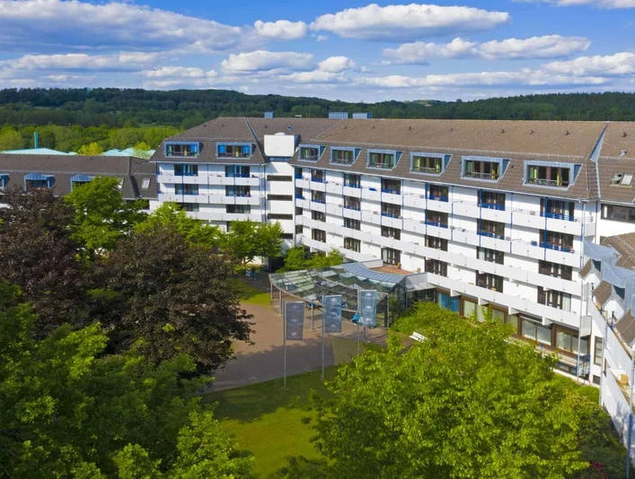 Blick auf die Caspar Heinrich Klinik, umgeben von Bäumen, mit fünfgeschossigem Gebäude und schöner Gartenanlage.