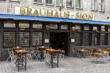 Brauhaus Sion Außengastronomie vor dem Brauhaus . An der Fassade steht in goldenen Buchstaben Brauhaus Sion.