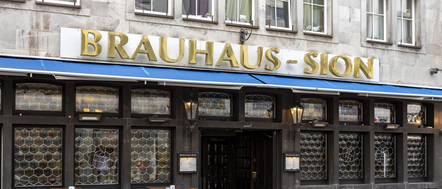 Außengastronomie vor dem Brauhaus . An der Fassade steht in goldenen Buchstaben Brauhaus Sion.