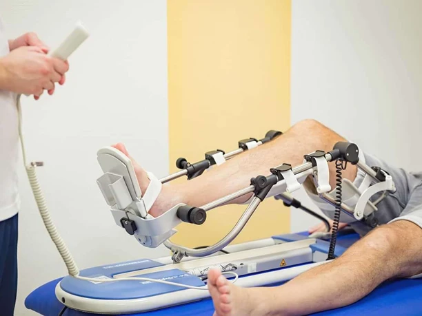 Bad Driburg_Gräfliche Kliniken_Marcus Klinik Ein Patient liegt auf einem Therapiegerät zum Kniebeugertraining, betreut von einer Fachperson.