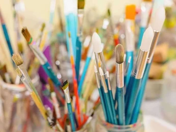 Mehrere farbenfrohe Malpinsel stehen in Glasgefäßen, die dicht aneinander gereiht sind.