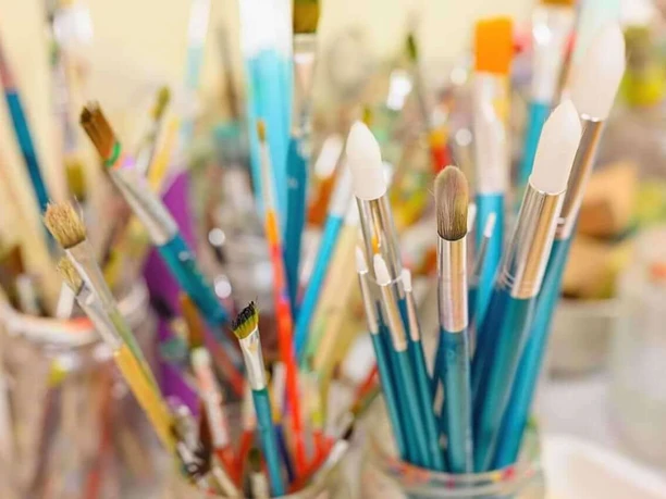 Mehrere farbenfrohe Malpinsel stehen in Glasgefäßen, die dicht aneinander gereiht sind.