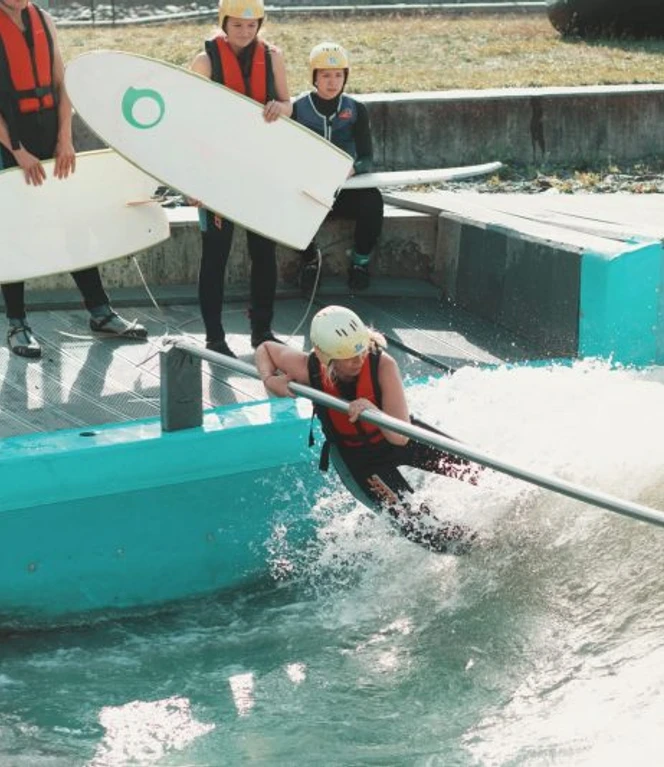 anna-kieselbach-64-800x533.jpg Personen beim Training auf einer künstlichen Surfwelle mit Surfbrettern und Schutzwesten.